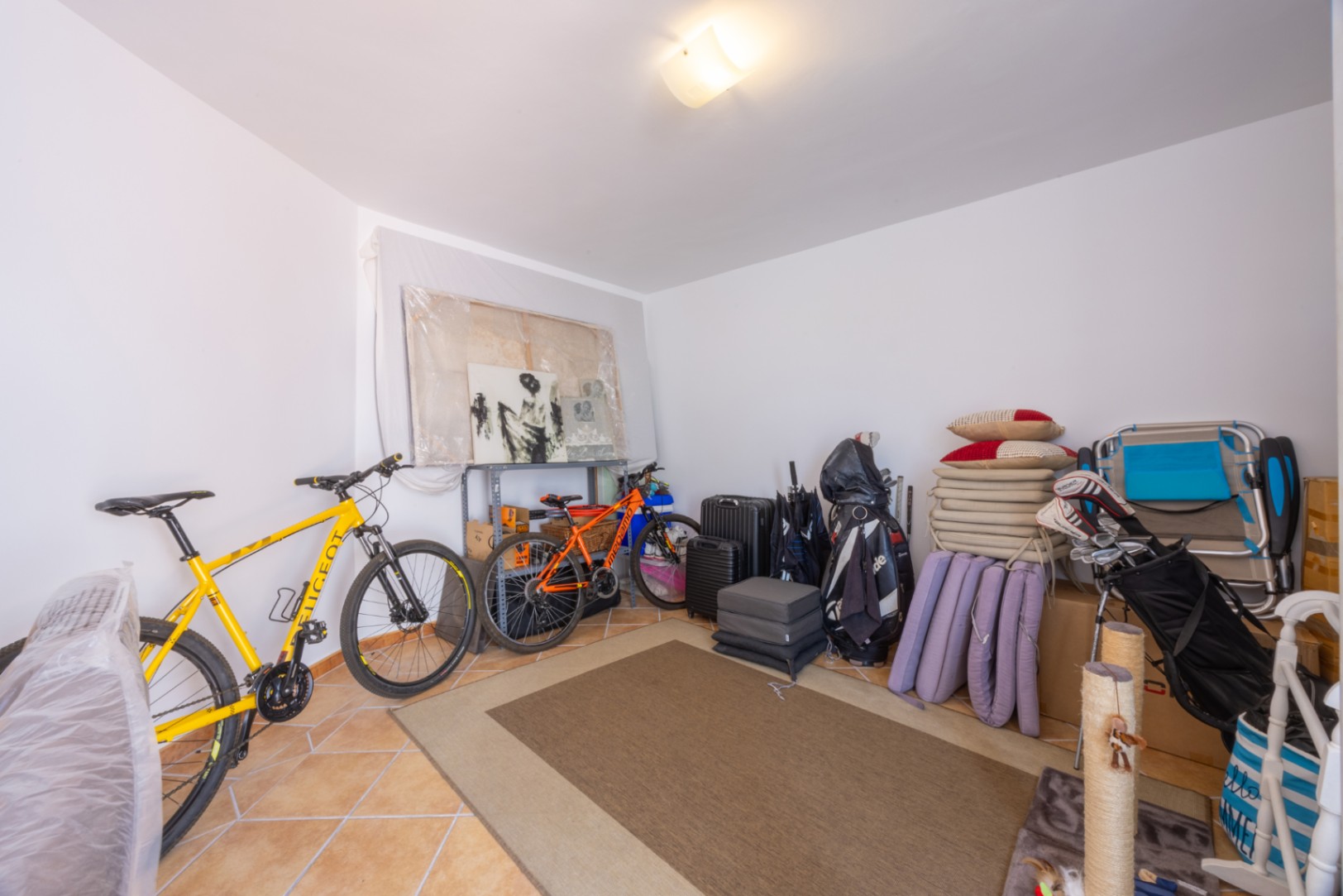 Pièce de rangement polyvalente avec sol carrelé, offrant un espace organisé pour les vélos, le matériel de sport et divers objets domestiques.