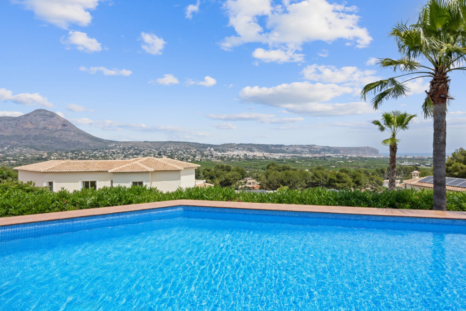 Piscine avec mosaïque bleue et bordure en terre cuite, offrant une vue panoramique sur la vallée et les montagnes environnantes.