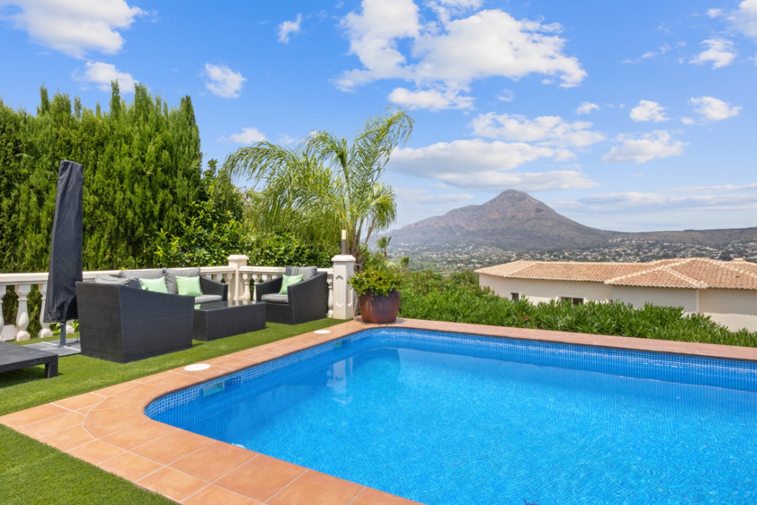 Piscine extérieure avec bordure en terre cuite, espace détente en gazon synthétique avec mobilier en rotin et vue panoramique sur les montagnes.