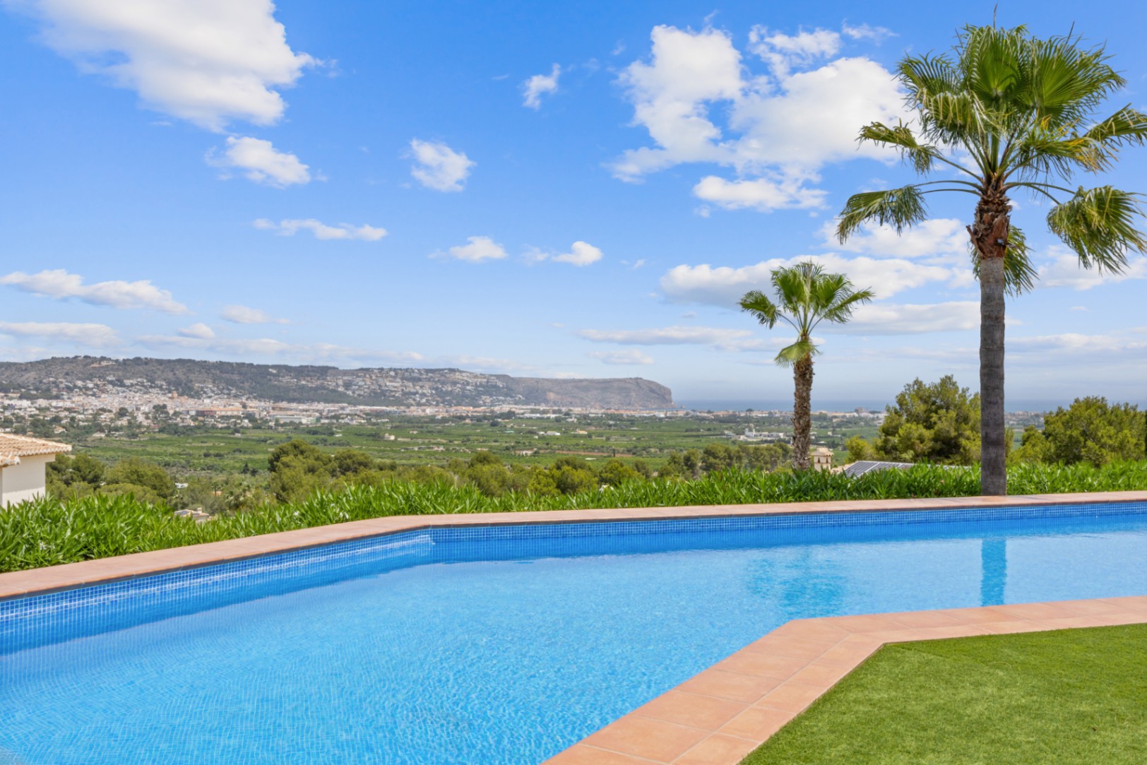 Piscine incurvée avec mosaïque bleue et bordure en terre cuite, offrant une vue panoramique sur la vallée et le paysage urbain lointain.