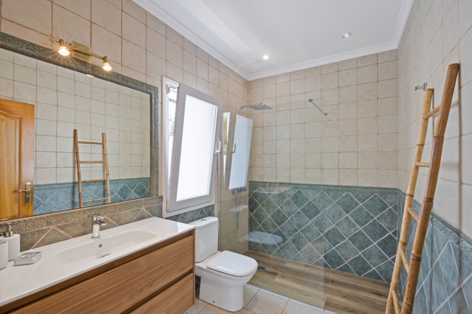 Salle de bain avec douche à l'italienne, carrelage mural vert en losanges, meuble sous-vasque en bois et échelle décorative en bambou pour les serviettes.