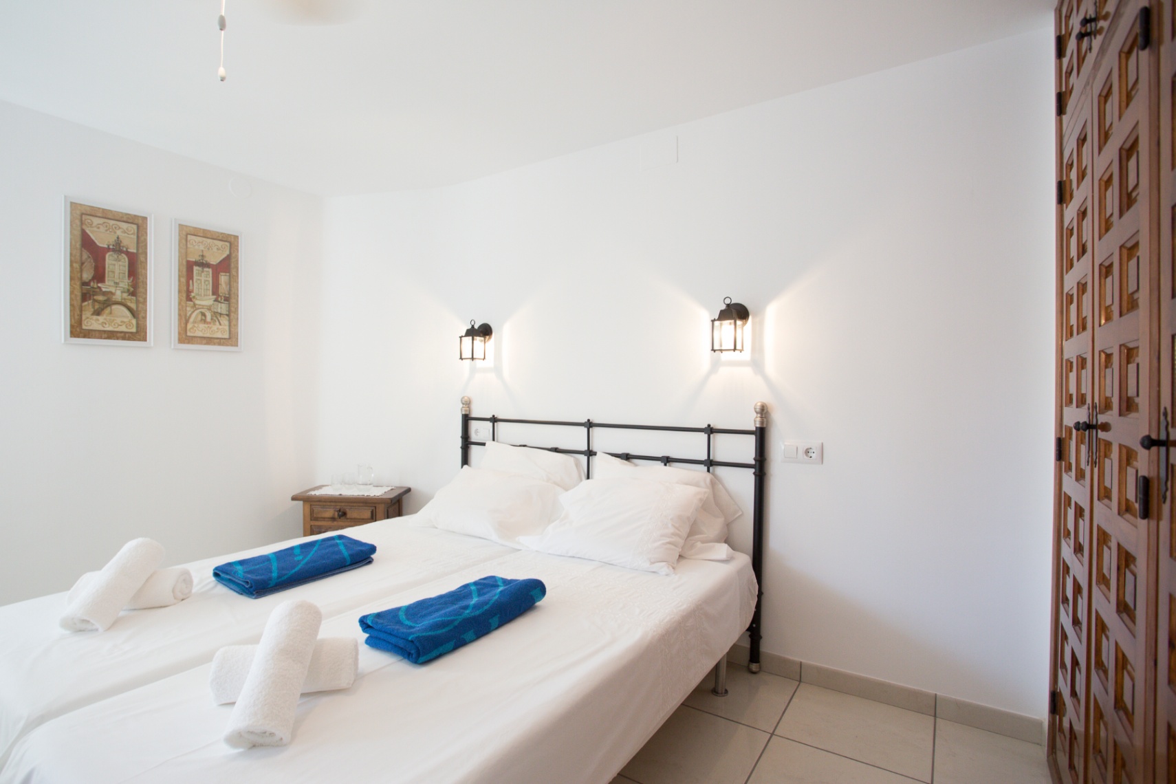 Chambre avec tête de lit en fer forgé noir, lits jumeaux, appliques murales style lanterne et une armoire en bois sculpté de style traditionnel.