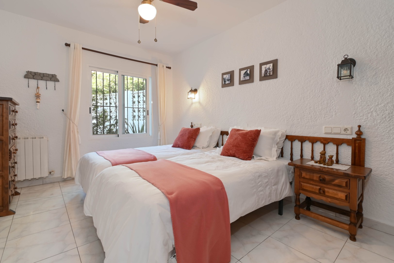Chambre lumineuse avec deux lits jumeaux, accents terracotta et mobilier en bois rustique. Les murs texturés et la fenêtre avec vue sur le jardin complètent l'espace.