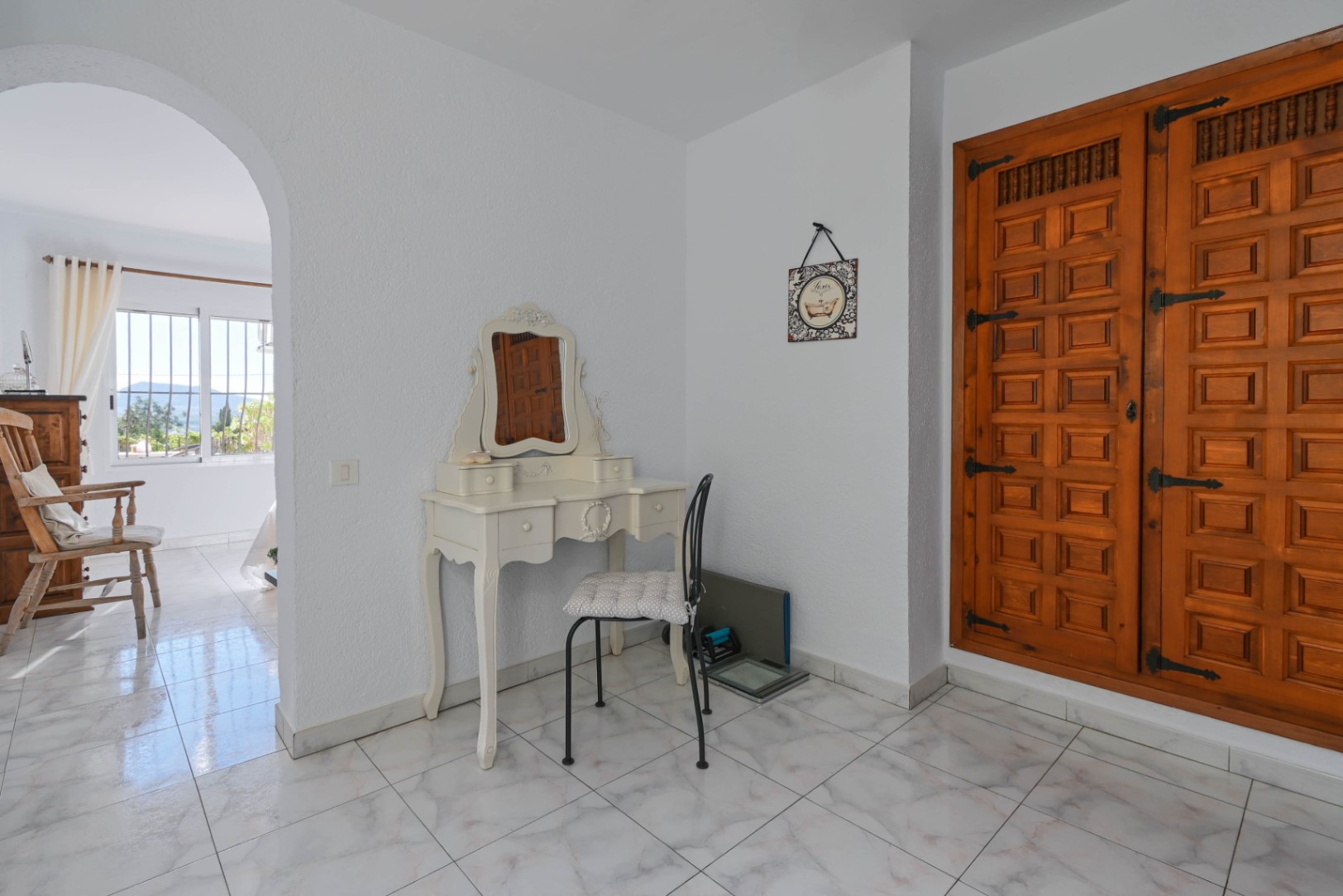 Coin coiffeuse avec table blanche de style vintage et grand placard intégré en bois sculpté doté de ferrures traditionnelles en fer noir.