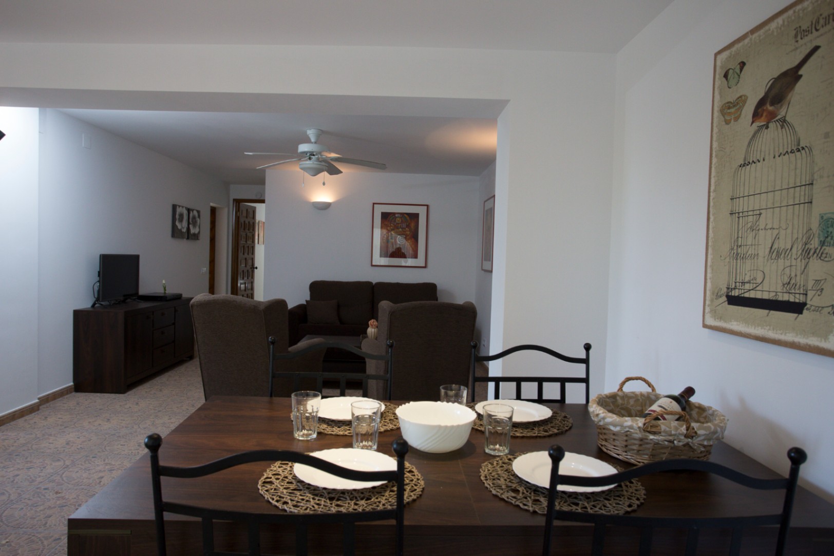 Espace ouvert avec salle à manger en bois sombre, chaises en métal noir, sol en carrelage à motifs et salon équipé d'un ventilateur de plafond et de canapés bruns.