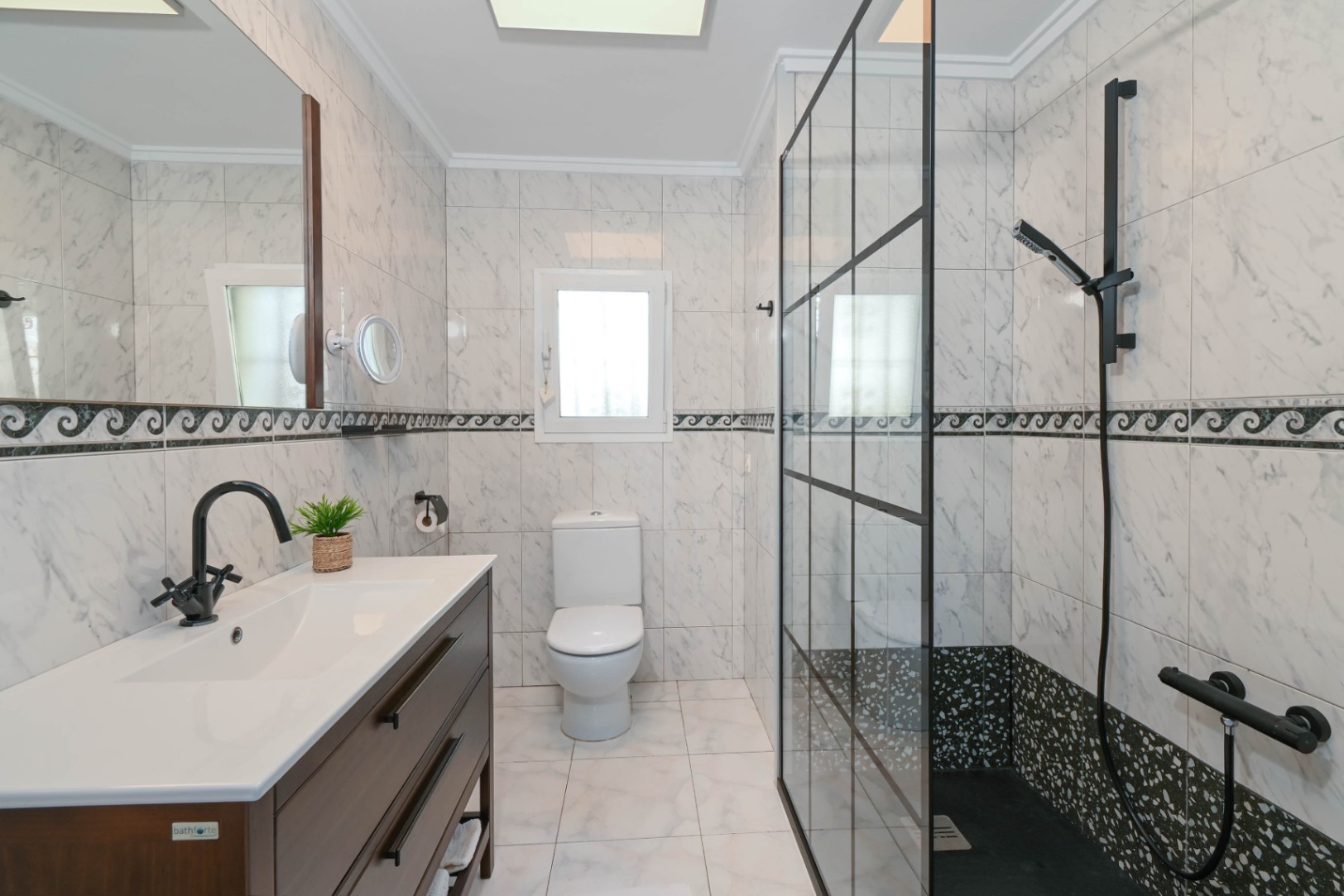 Salle de bain moderne avec carrelage effet marbre, meuble sous-vasque sombre et douche à l'italienne dotée d'une paroi vitrée à cadre noir.