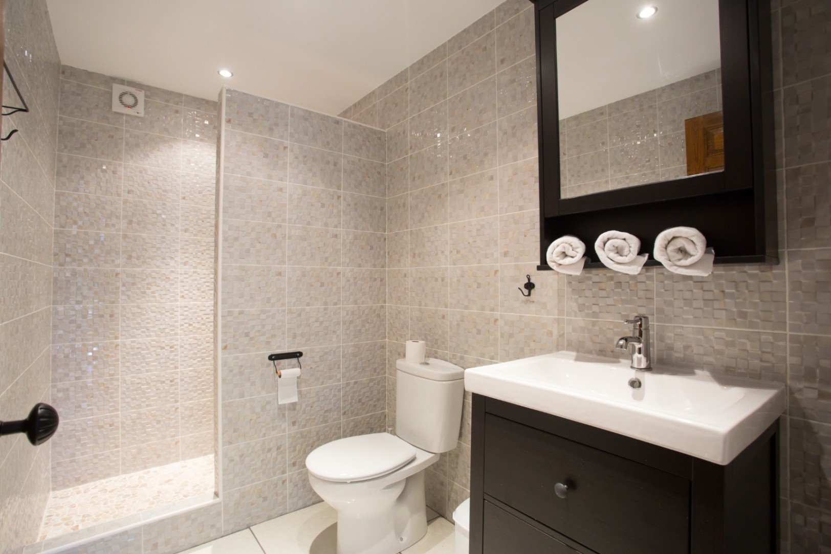 Salle de bain moderne avec douche à l'italienne en mosaïque, meuble vasque en bois sombre et armoire de toilette assortie.