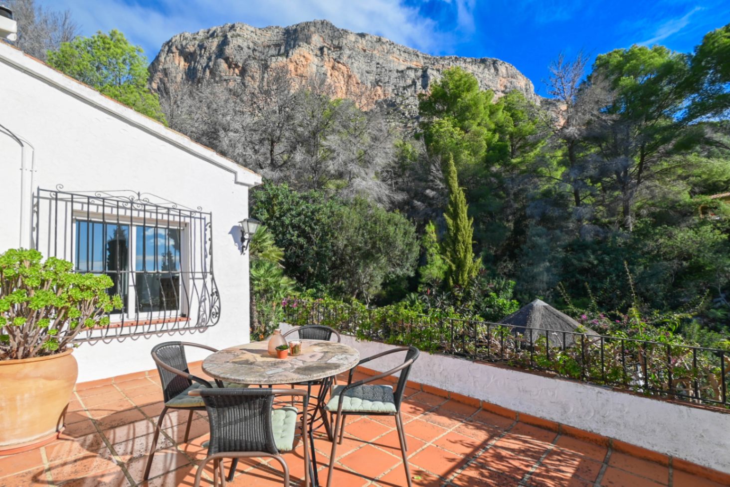 Terrasse en terre cuite avec mobilier de jardin en pierre, offrant une vue imprenable sur la forêt environnante et la paroi rocheuse.