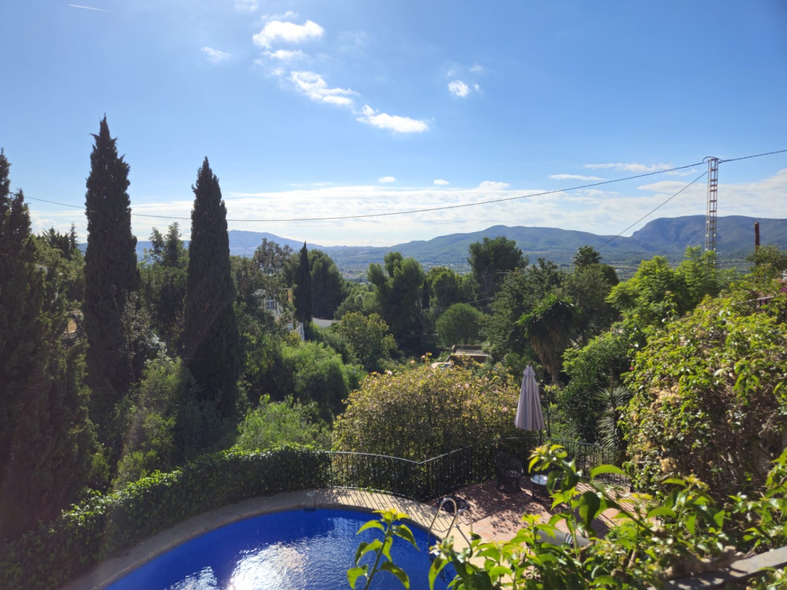 Vue surélevée d'une piscine courbée et d'une terrasse en terre cuite, entourée de cyprès avec vue panoramique sur la vallée et les montagnes.