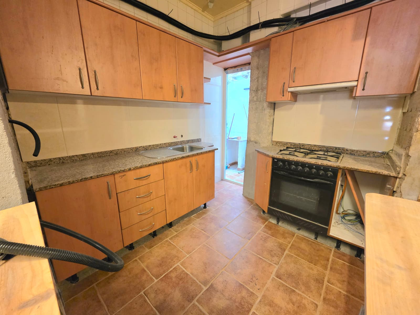 Cuisine avec placards en finition bois, plans de travail en granit et sol en terre cuite. Équipée d'une plaque de cuisson au gaz et d'un accès vers l'extérieur.