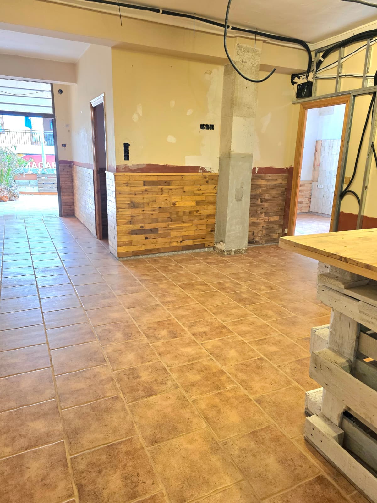 Espace intérieur avec carrelage en terre cuite, soubassement en bois de récupération et câblage apparent, offrant un potentiel de rénovation.