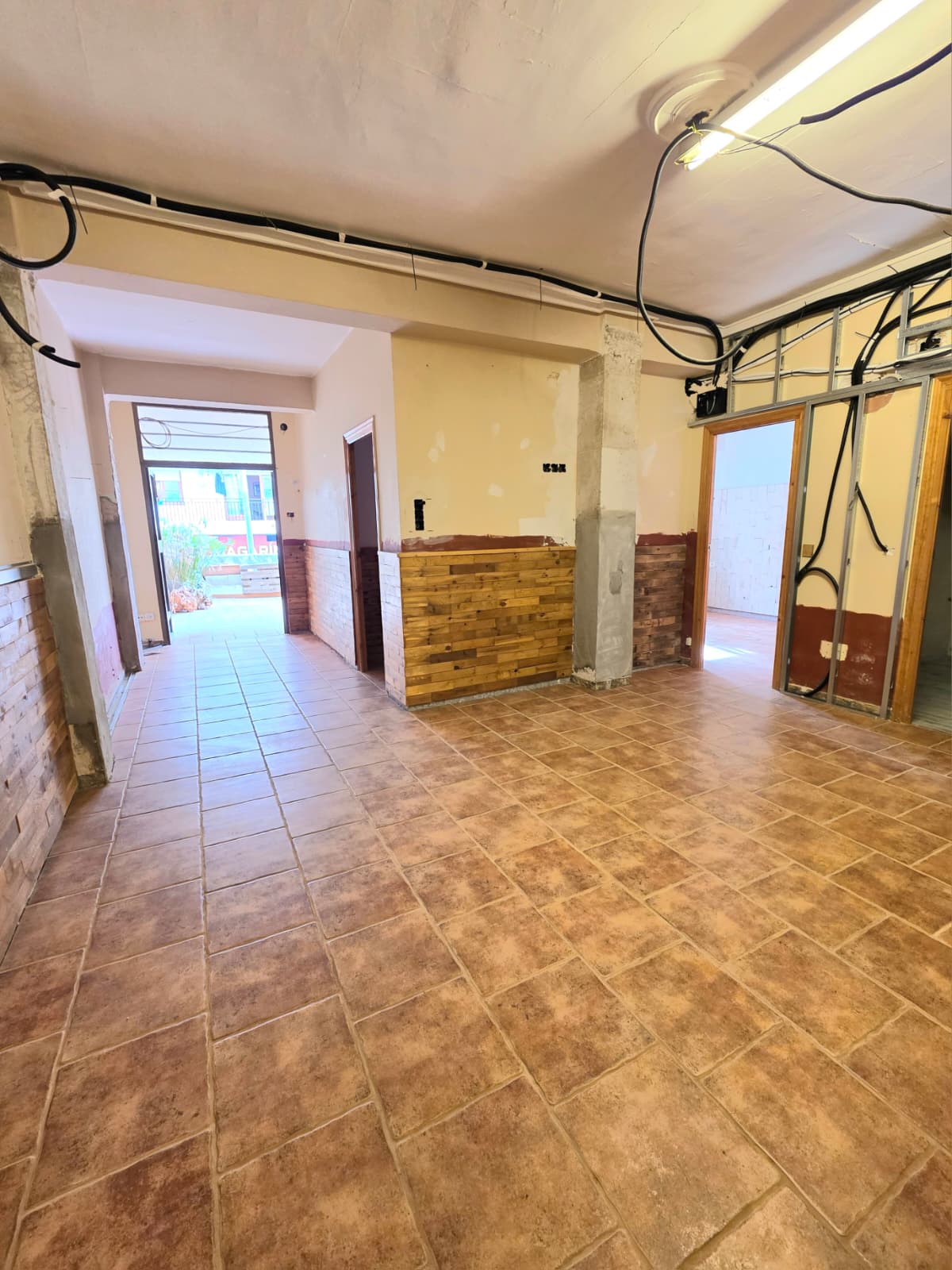 Espace intérieur en rénovation avec sol en grès cérame, lambris en bois partiel et installations électriques apparentes avec ossature métallique.