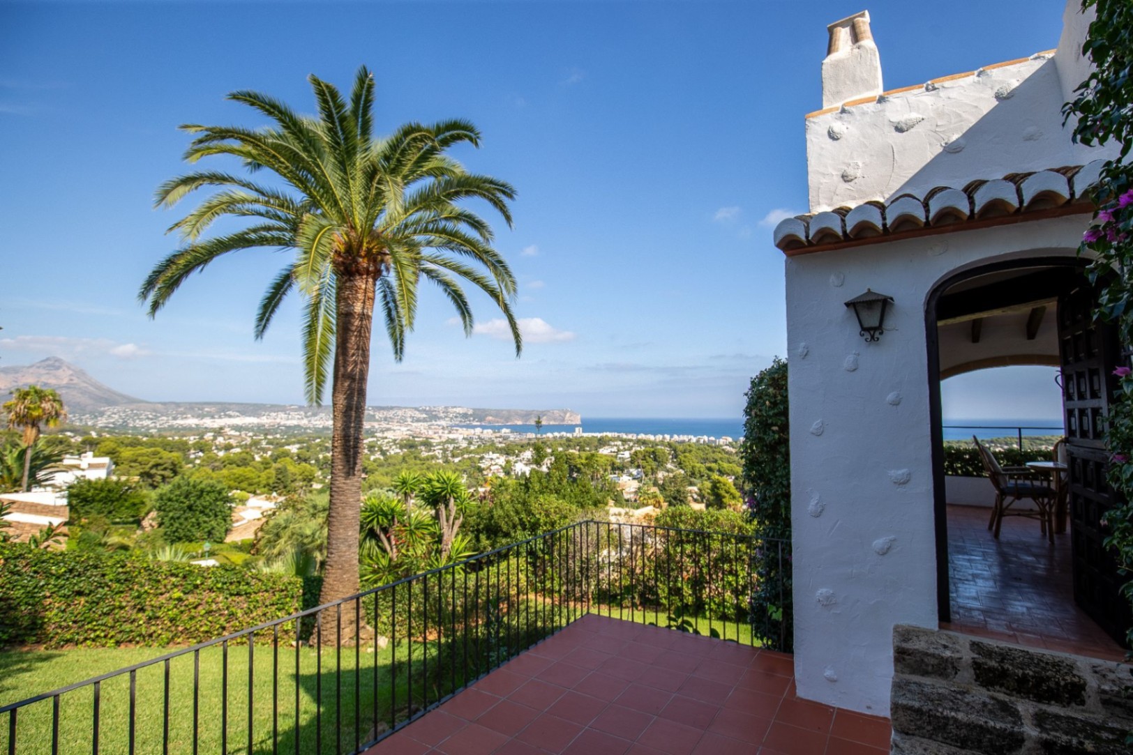 Terrasse en terre cuite offrant une vue panoramique sur le littoral méditerranéen, avec un palmier imposant et une façade traditionnelle en stuc blanc.
