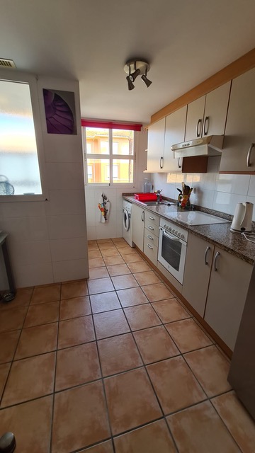 Cuisine équipée avec sol en grès cérame, plan de travail en granit et meubles crème. Comprend des appareils intégrés et une fenêtre offrant une lumière naturelle.