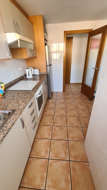 Cuisine fonctionnelle avec plan de travail en granit moucheté, meubles blancs et sol en grès. Comprend un four intégré et une hotte.