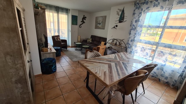 Espace de vie ouvert comprenant un coin repas avec table en bois à motifs chevrons, un salon avec canapé en cuir et un sol en carrelage de terre cuite.