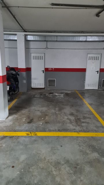 Place de parking numérotée dans un garage souterrain avec sol en béton, marquage au sol jaune et accès direct aux portes de service.