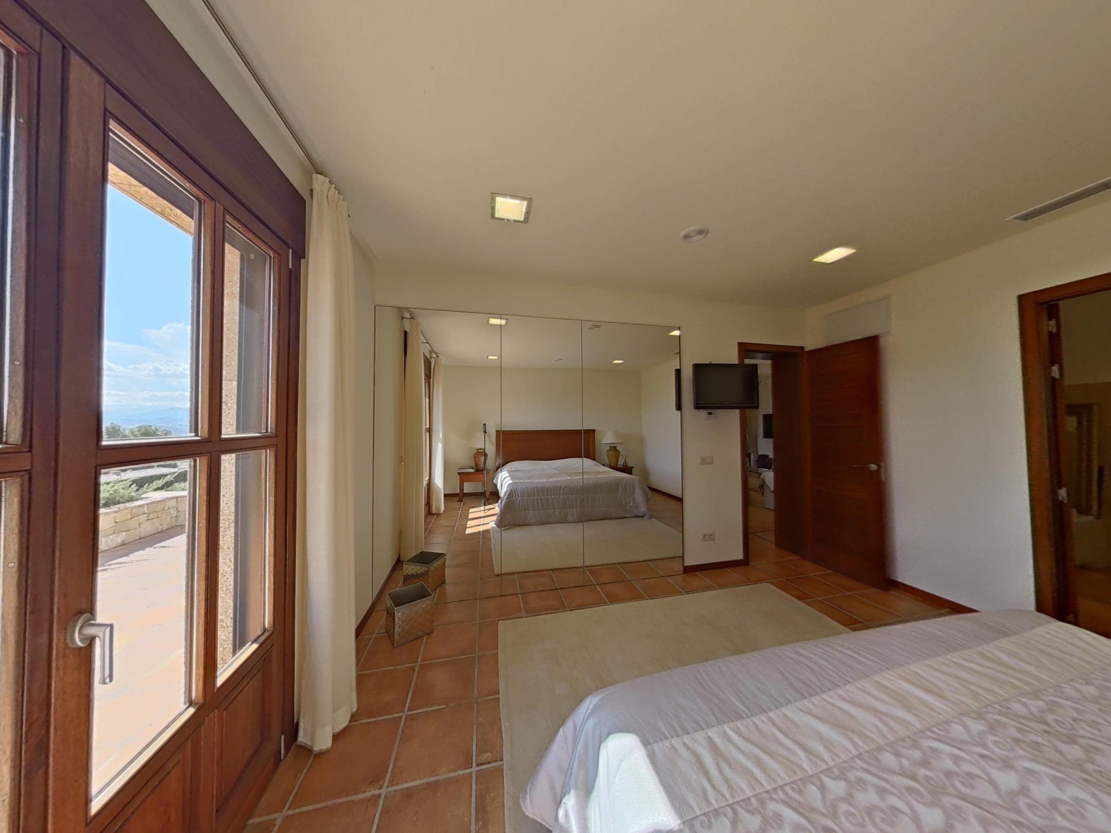 Chambre avec carrelage en terre cuite, penderie à miroirs et accès à une terrasse extérieure par des portes vitrées en bois.