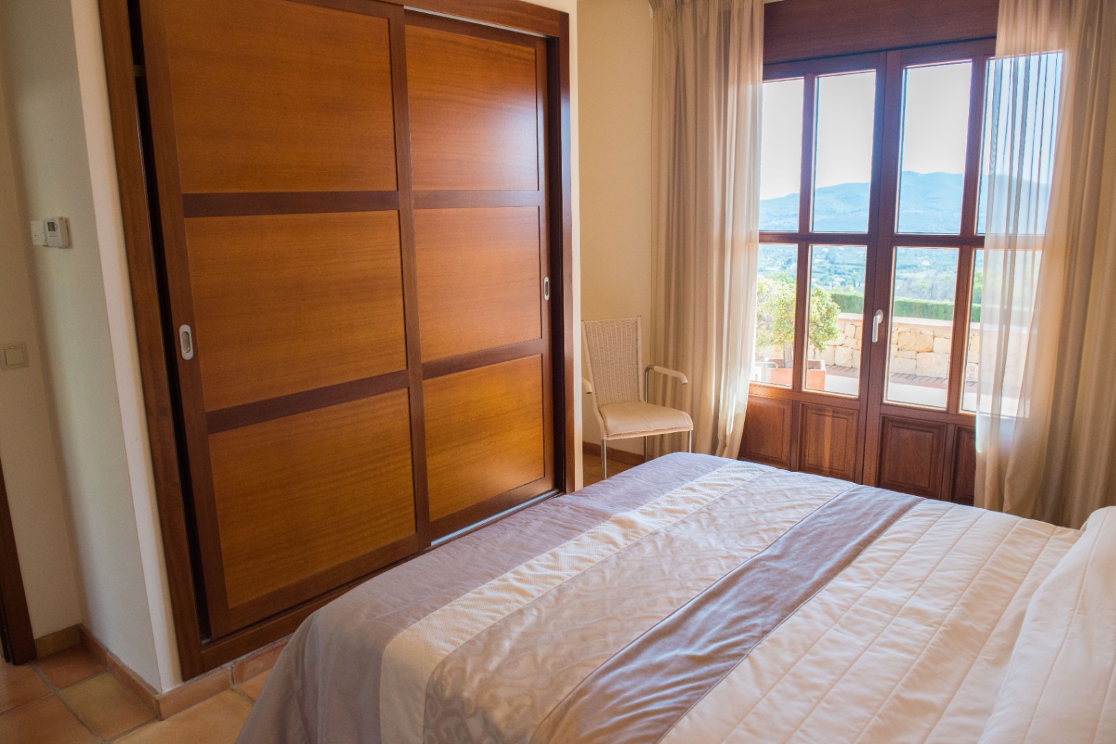 Chambre avec grand placard intégré en bois, portes coulissantes et accès à une terrasse offrant une vue panoramique sur les montagnes.