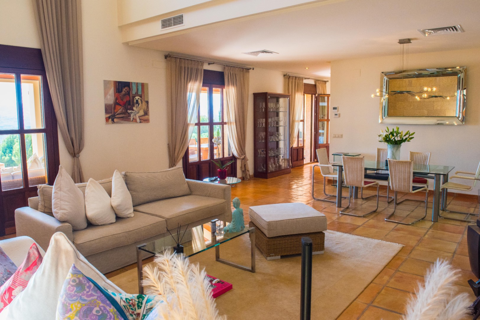 Espace de vie ouvert avec sol en terre cuite, coin repas avec table en verre et salon lumineux donnant sur une terrasse par des portes-fenêtres.