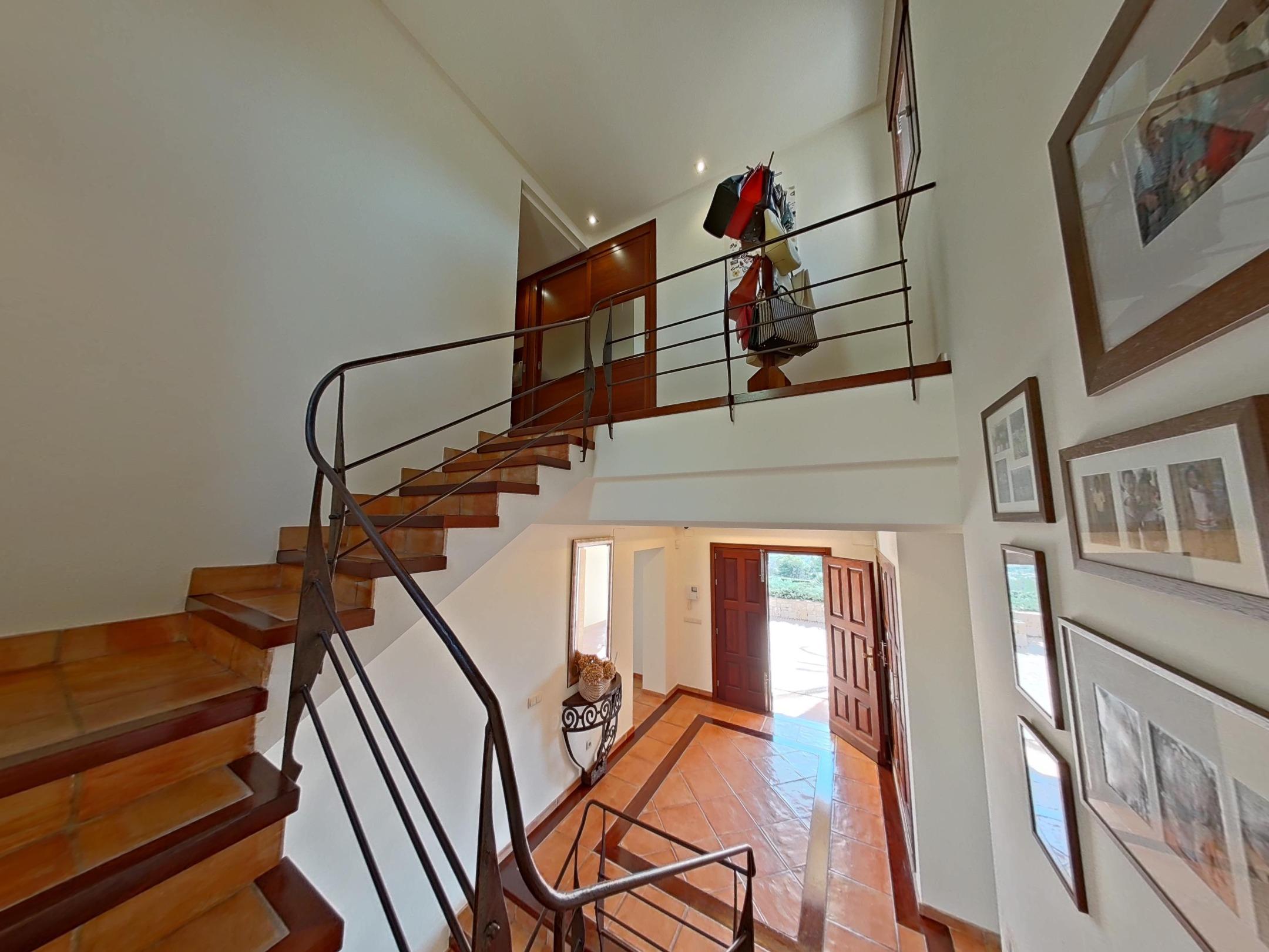 Hall d'entrée vu depuis l'escalier, doté d'un sol en terre cuite avec bordures, d'une rampe en fer forgé et d'une double porte en bois massif.