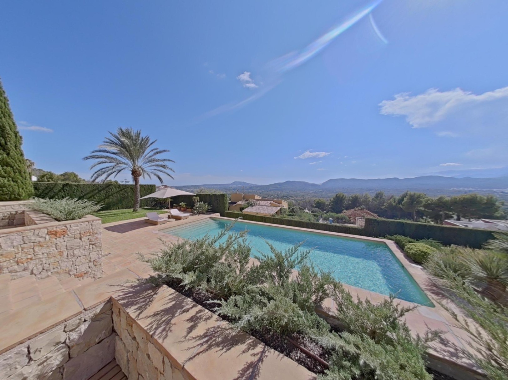 Piscine extérieure avec terrasse en pierre et vue panoramique sur la vallée. Comprend des bains de soleil, un palmier et un jardin méditerranéen.