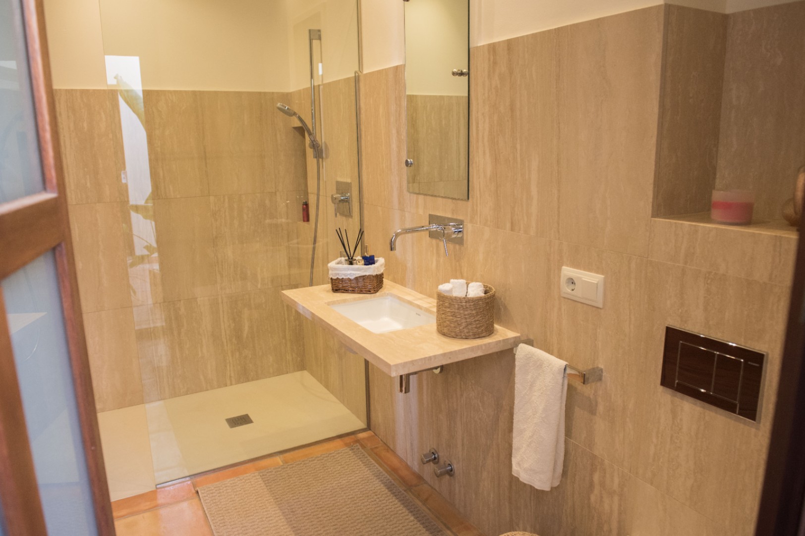 Salle de bain moderne avec douche à l'italienne, vasque suspendue en pierre naturelle et robinetterie murale sur un revêtement en travertin beige.