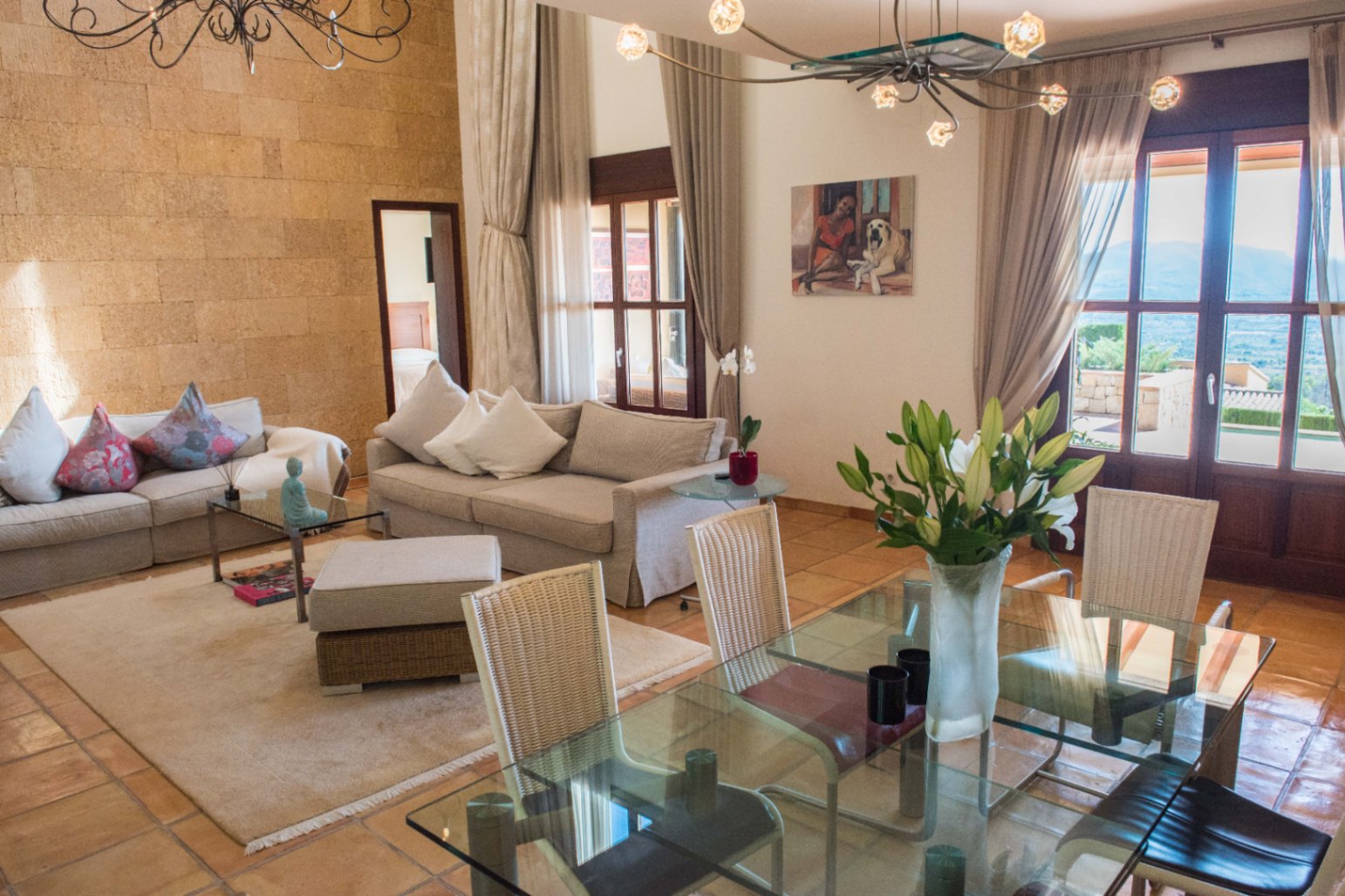 Séjour et salle à manger à aire ouverte avec mur en pierre apparente, sol en terre cuite et grandes baies vitrées ouvrant sur l'extérieur.