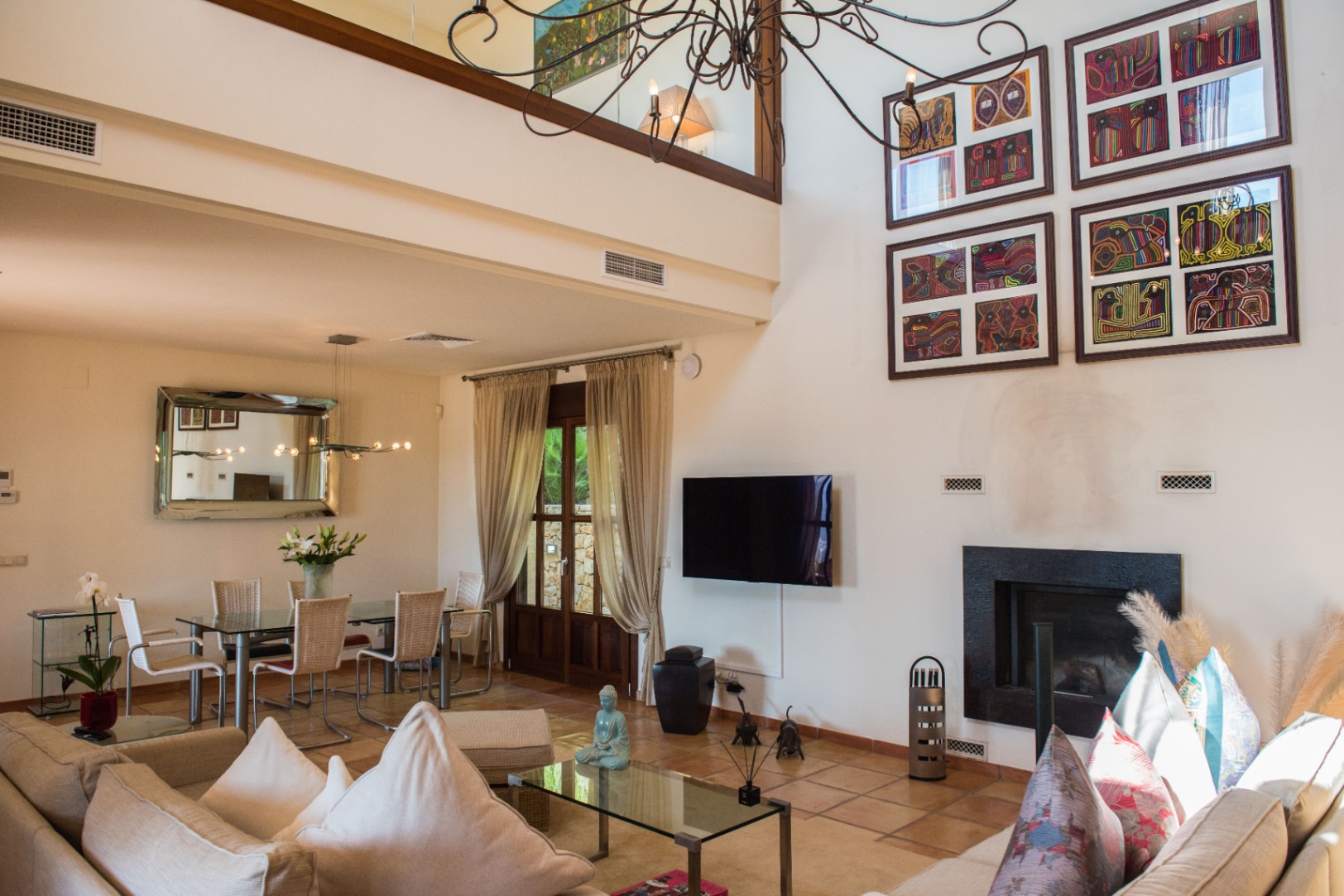 Séjour spacieux à double hauteur avec sol en terre cuite, cheminée moderne, coin repas avec table en verre et mezzanine surplombant l'espace de vie.