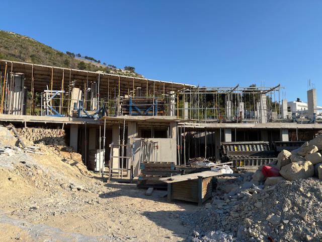 Villa en cours de construction révélant sa structure en béton armé, ses étais métalliques et ses coffrages en bois sur un terrain en pente.