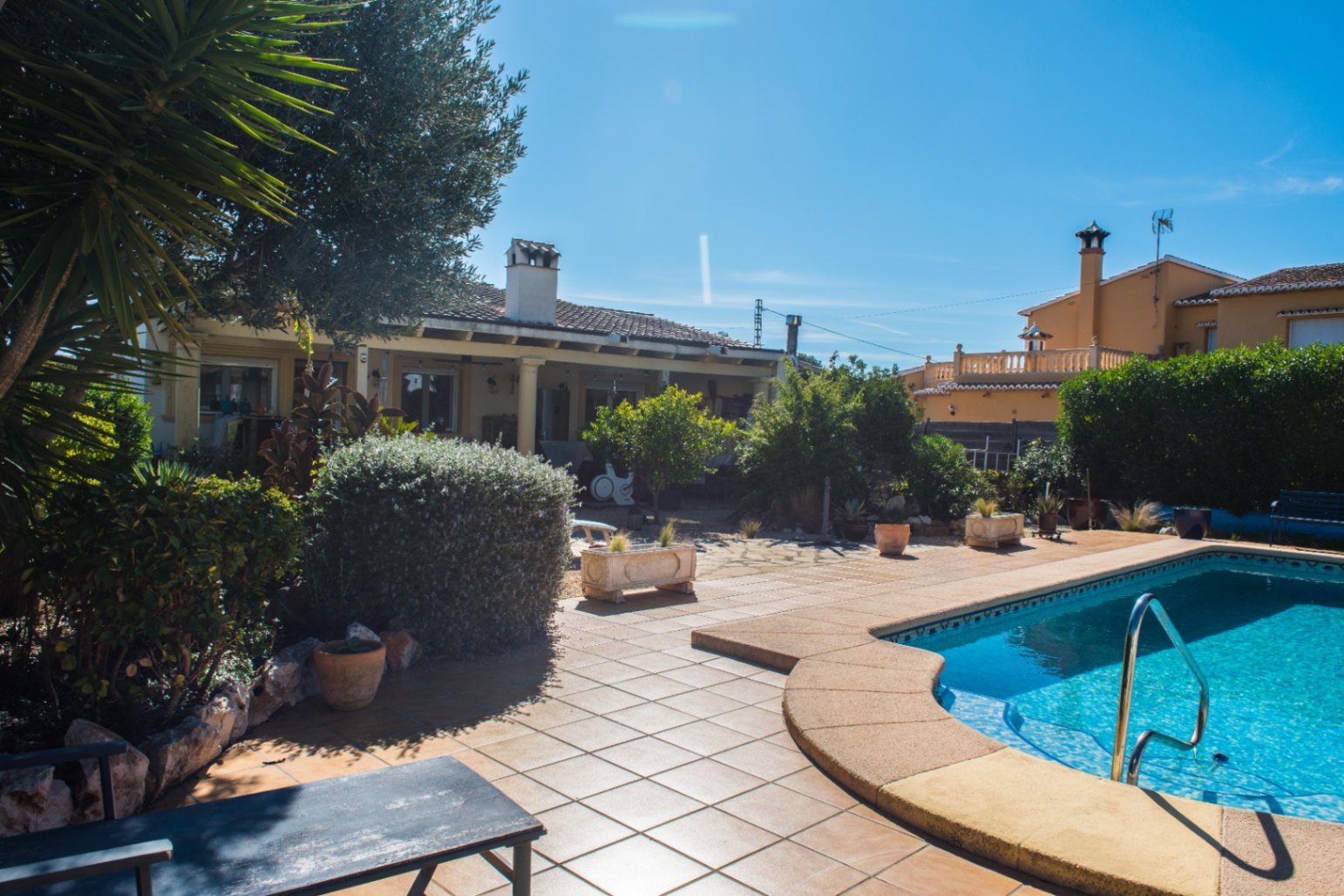 Espace piscine extérieure avec dallage en terre cuite, entouré d'un jardin méditerranéen arboré et d'une terrasse couverte à colonnes.