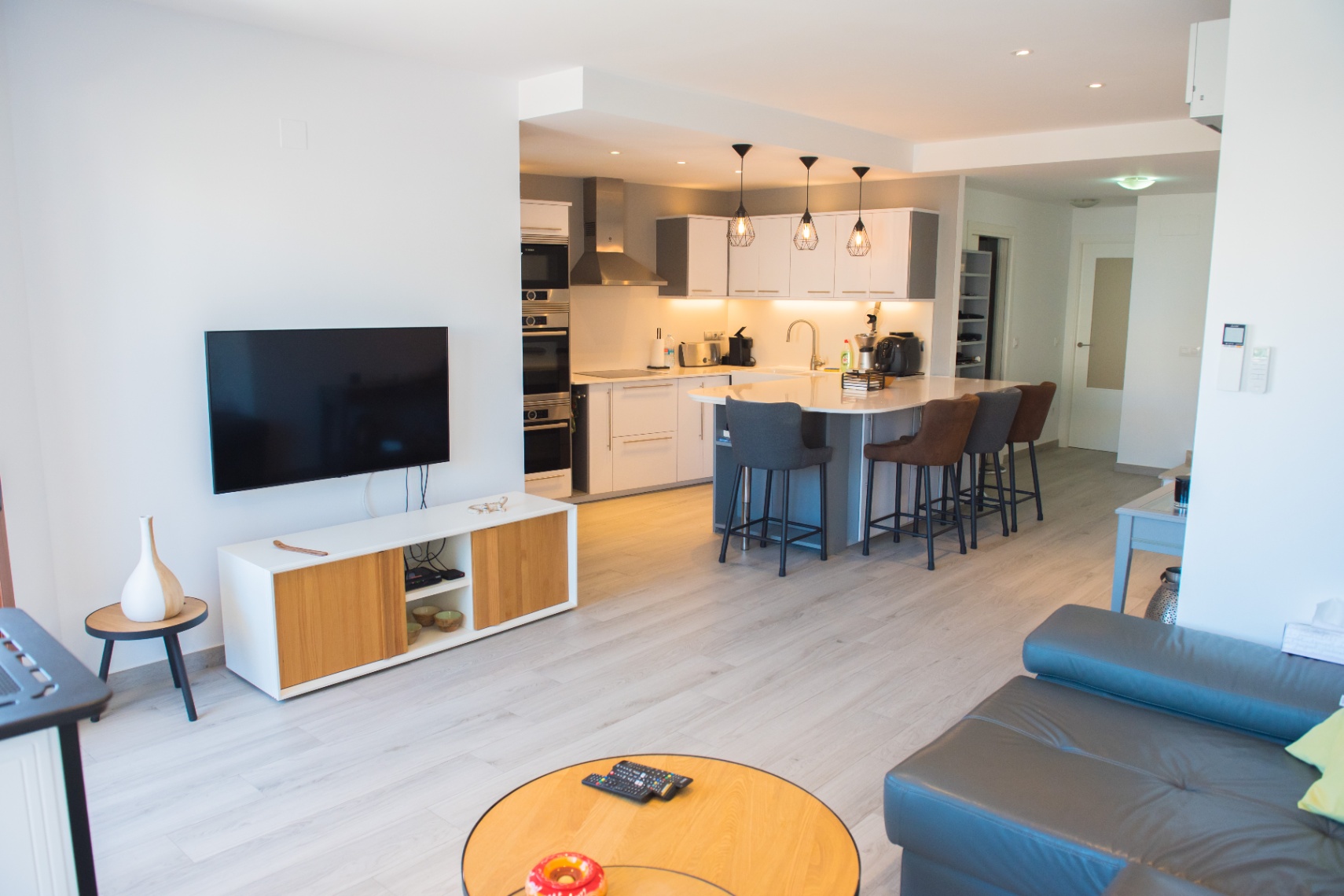 Espace de vie ouvert avec cuisine moderne, îlot central blanc, électroménager intégré et salon lumineux doté d'un sol en bois clair et d'un mobilier épuré.