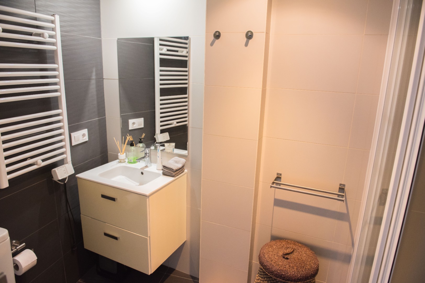 Salle de bain moderne avec meuble vasque suspendu, radiateur sèche-serviettes blanc et carrelage mural contrasté gris et crème.