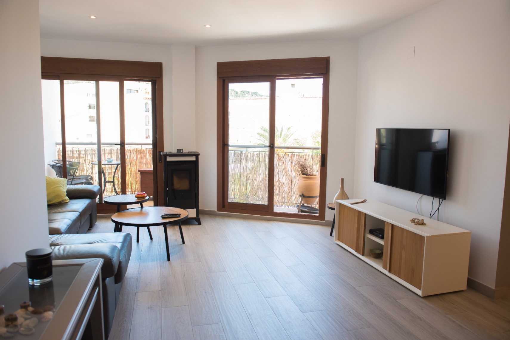 Séjour moderne avec canapé en cuir gris, poêle à granulés et tables basses en bois. De grandes baies vitrées coulissantes offrent une luminosité naturelle.