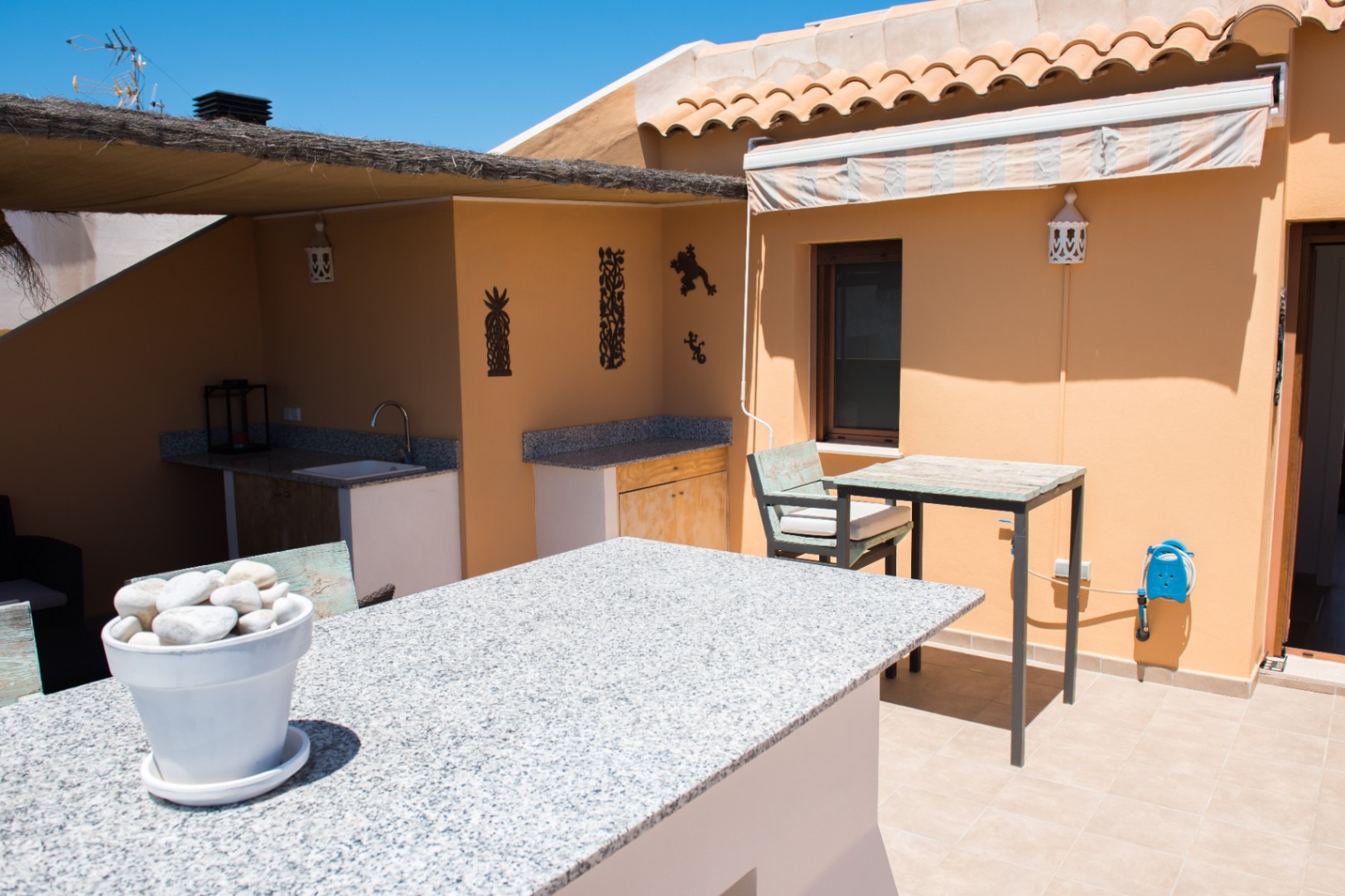 Terrasse extérieure avec bar en granit, coin évier intégré et rangements en bois rustique sous un auvent en chaume.