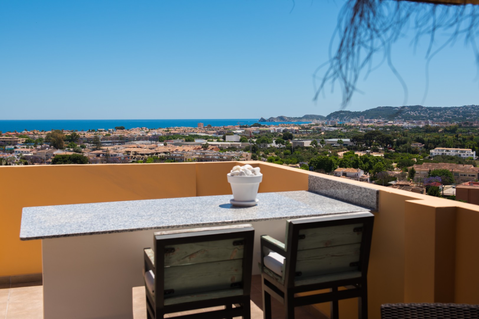 Terrasse surélevée avec bar en granit et sièges en bois, offrant une vue panoramique sur la ville côtière et la mer Méditerranée par temps clair.