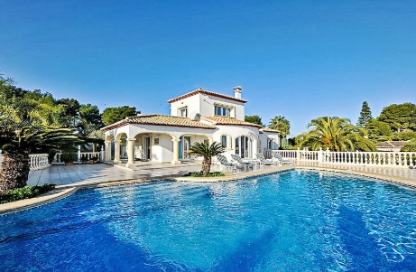 Vue extérieure de la villa avec piscine privée, vaste terrasse carrelée et naya à arcades. La façade blanche et les toits en terre cuite s'intègrent au jardin méditerranéen.