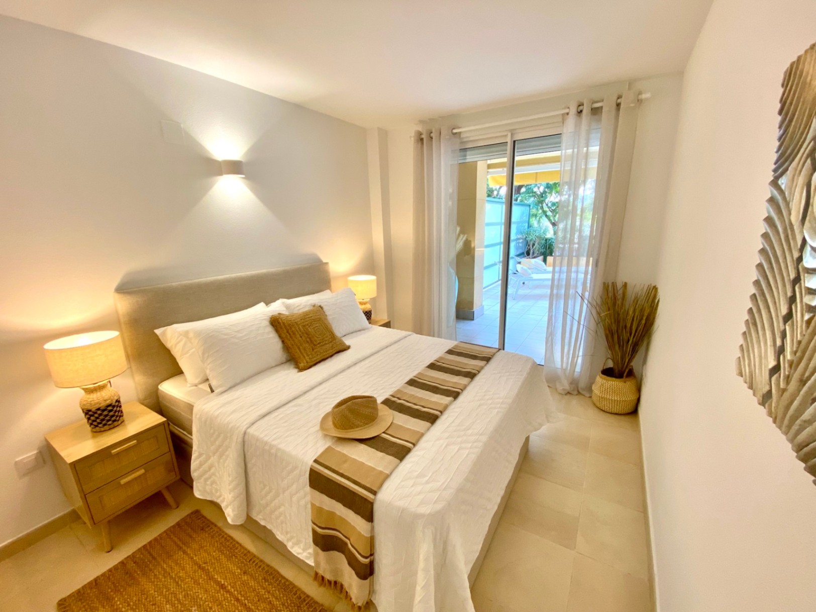 Chambre moderne avec lit double, tables de chevet en bois et accès direct à une terrasse privée par de grandes baies vitrées coulissantes.