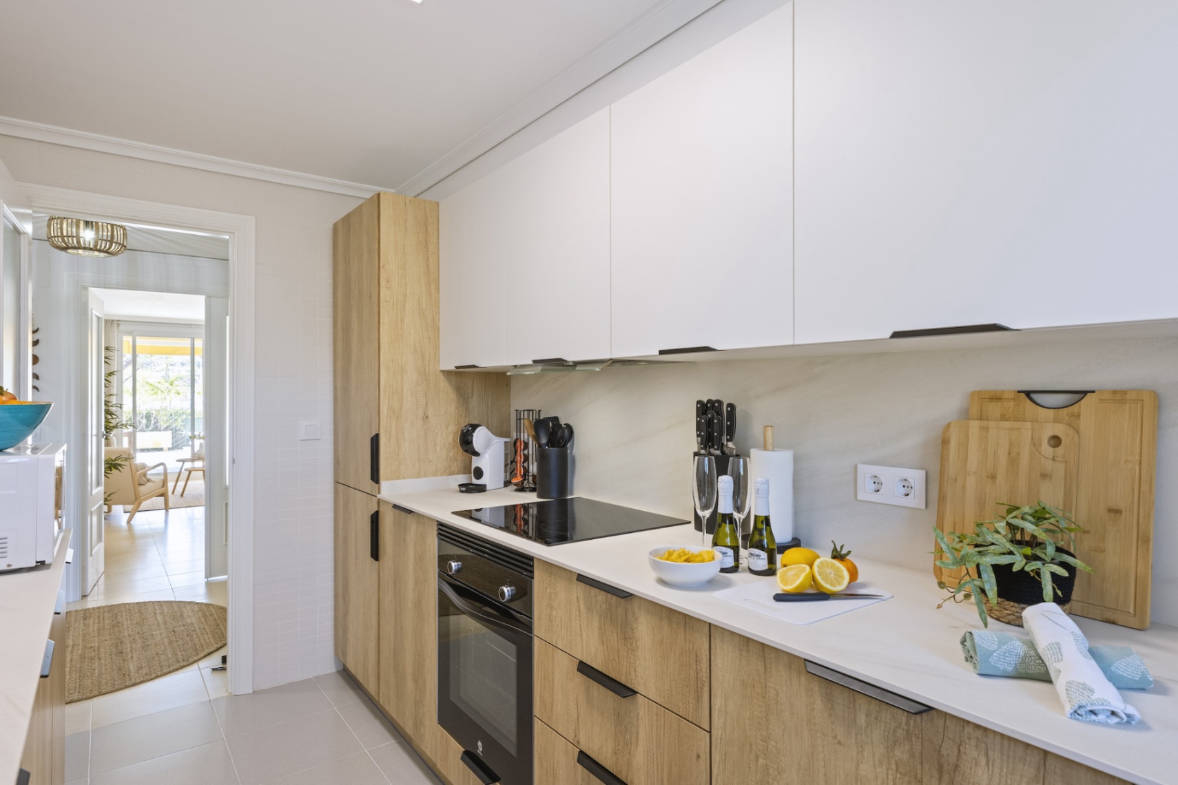 Cuisine moderne avec des armoires bicolores en blanc et bois naturel. Équipée d'une plaque à induction, d'un four intégré et de plans de travail en pierre blanche.