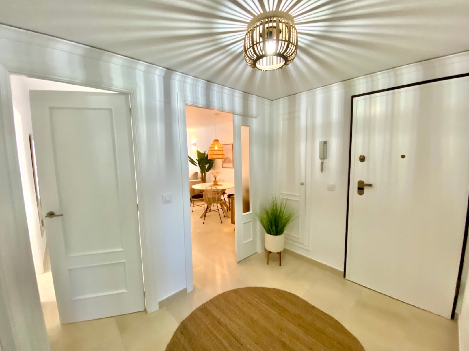 Entrée lumineuse avec une suspension en osier créant des jeux d'ombres, des portes blanches et un aperçu de la salle à manger.