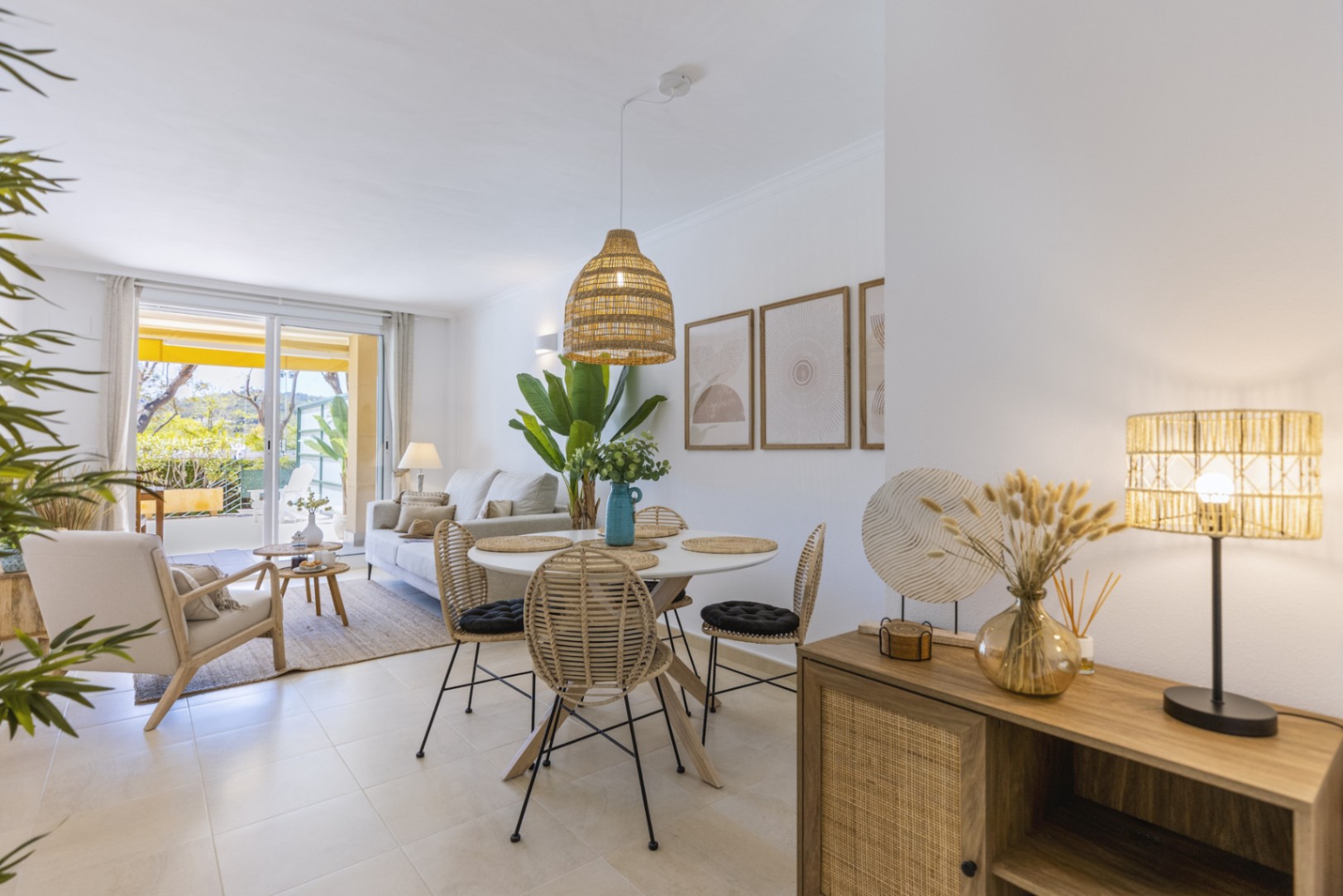 Espace de vie ouvert comprenant un coin repas avec chaises en rotin, une suspension en fibres naturelles et un salon ouvrant sur une terrasse ensoleillée.