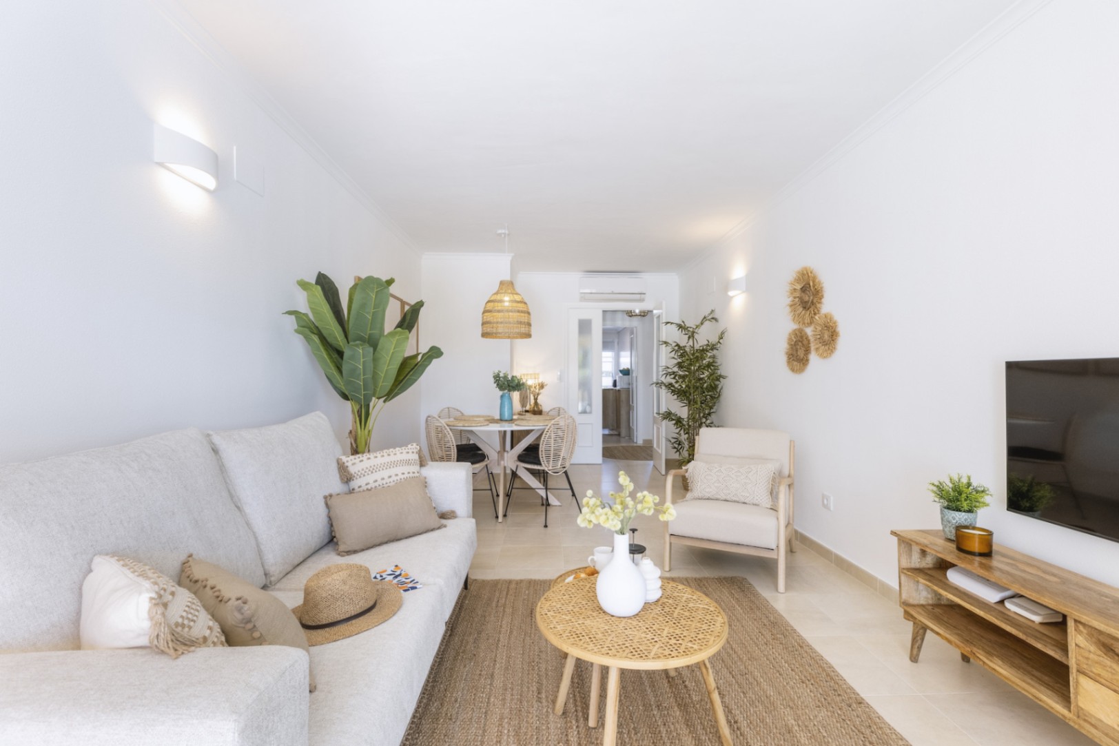 Salon-salle à manger lumineux aux tons neutres, avec canapé en tissu, table basse en osier et tapis en fibres naturelles sous des appliques murales.