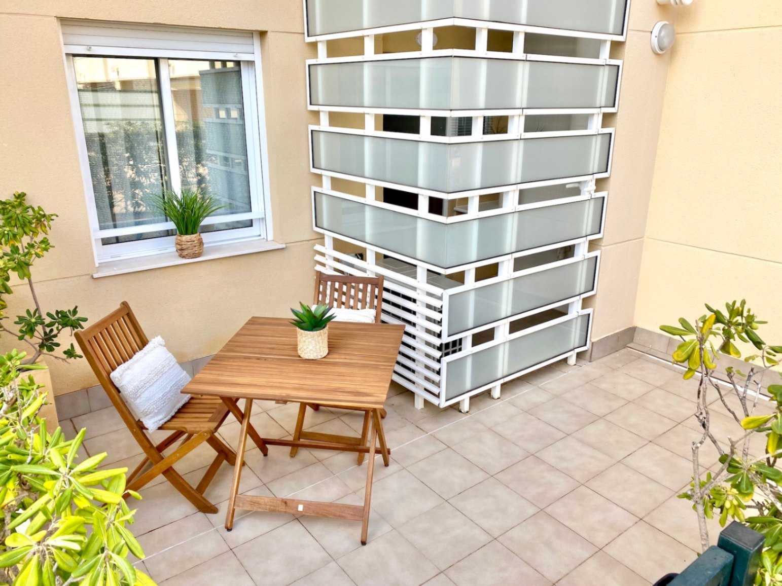 Terrasse privée avec carrelage au sol, mobilier de jardin pliant en bois et une paroi de séparation moderne en verre dépoli et métal blanc.