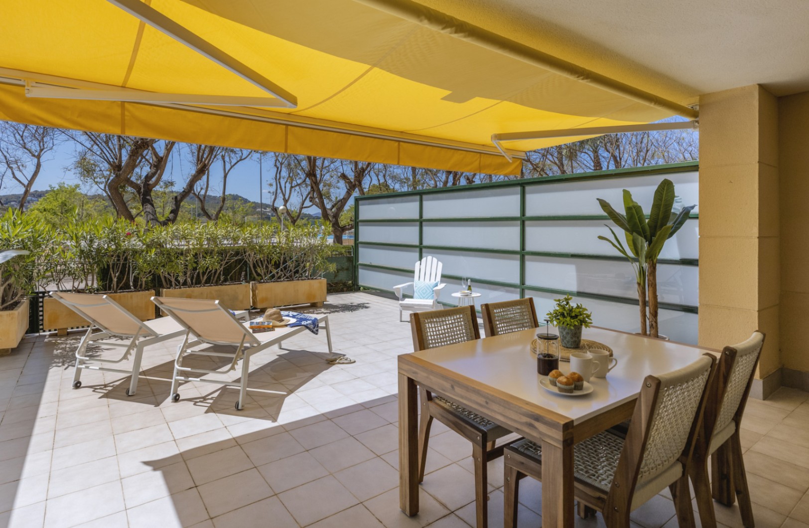 Terrasse privée avec store banne jaune, table à manger en bois et espace solarium avec transats blancs, protégée par des parois d'intimité.