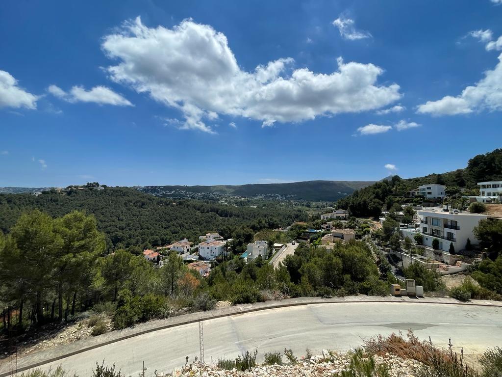 Vue panoramique surélevée d'une vallée méditerranéenne avec des villas blanches nichées dans des collines de pins sous un ciel bleu parsemé de nuages.