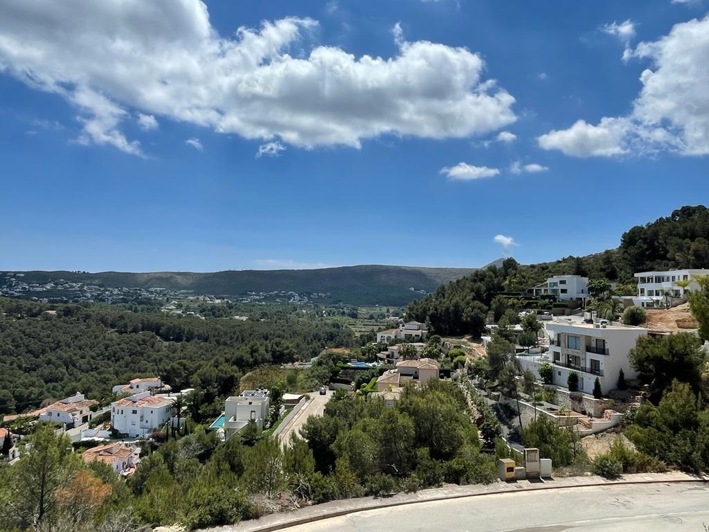 Vue surélevée d'une vallée méditerranéenne avec des villas blanches nichées dans une pinède dense sous un ciel azur.