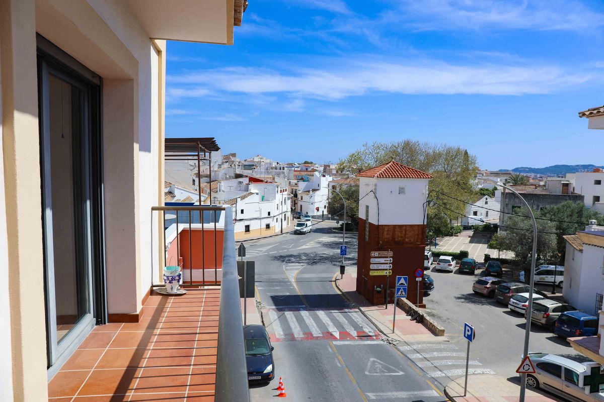 Balcon avec carrelage en terre cuite et garde-corps métallique offrant une vue sur un carrefour urbain et des bâtiments blancs méditerranéens.