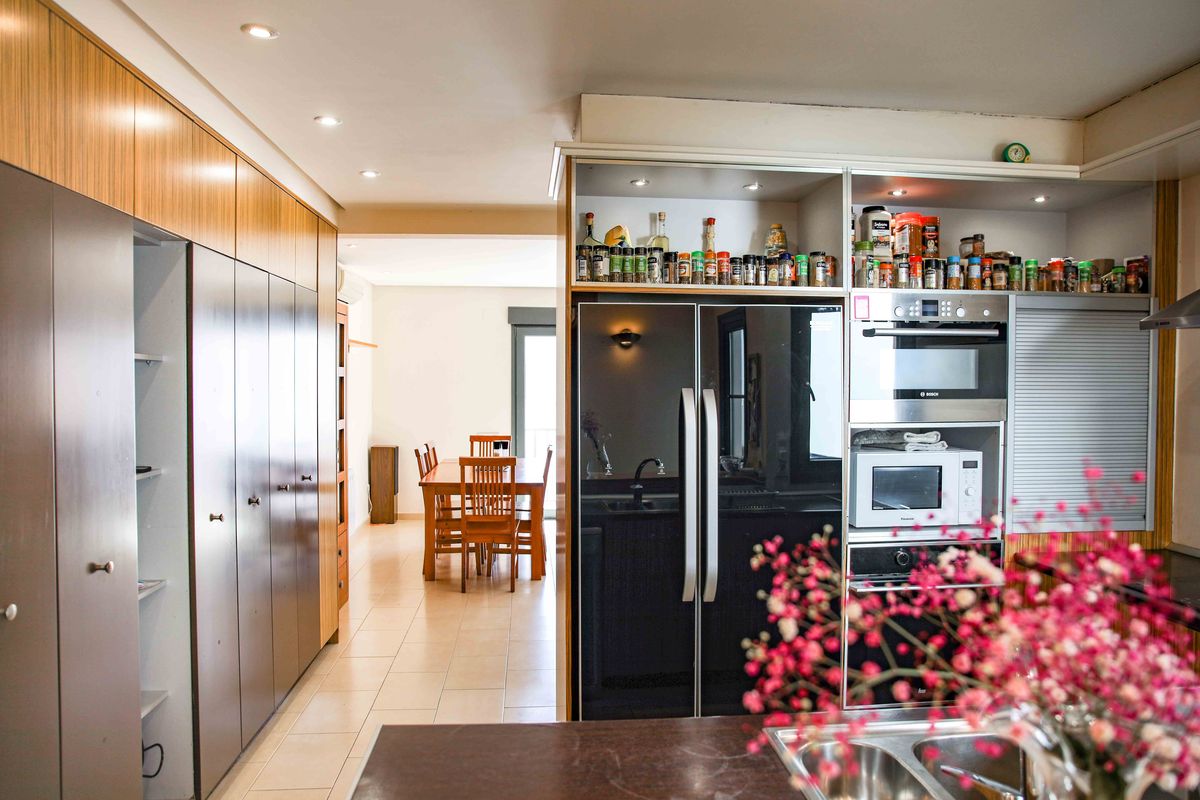 Cuisine moderne équipée d'appareils intégrés, d'un réfrigérateur noir à double porte et de nombreux rangements toute hauteur menant à la salle à manger.