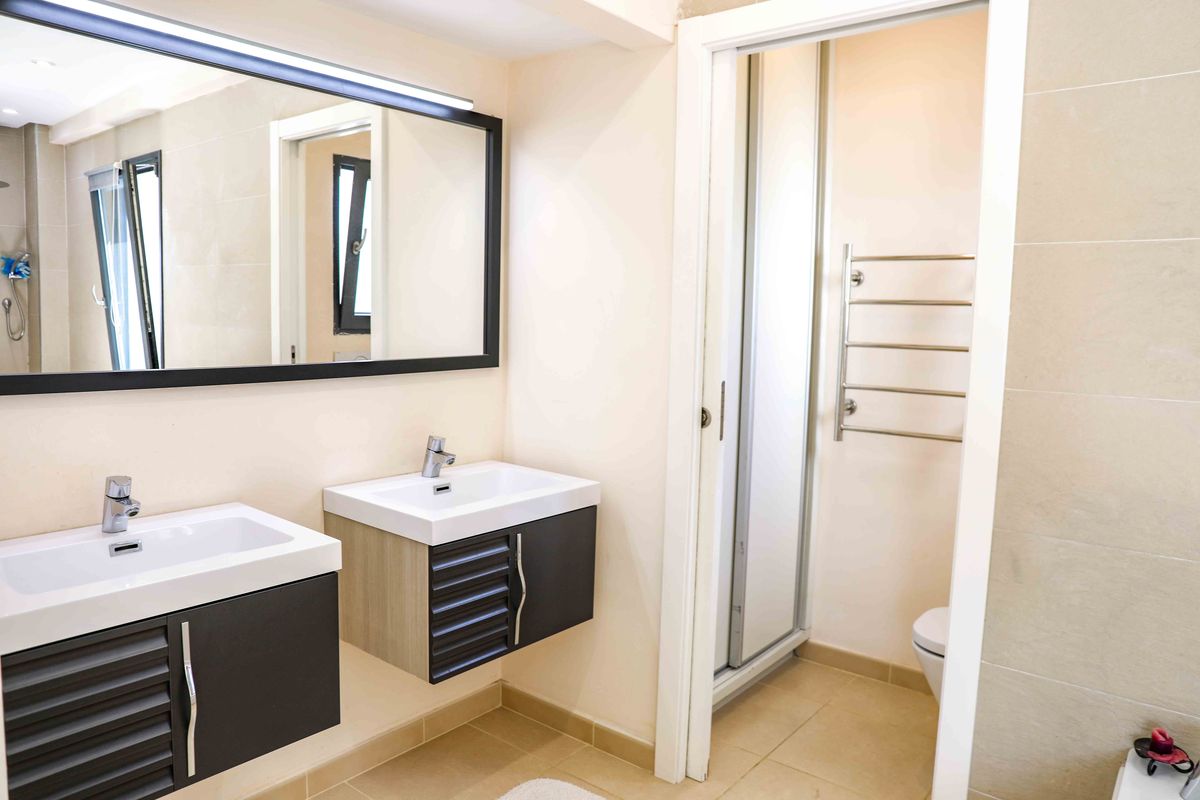 Salle de bain moderne avec double vasque, meubles texturés sombres, grand miroir à cadre noir et espace toilettes séparé avec sèche-serviettes.