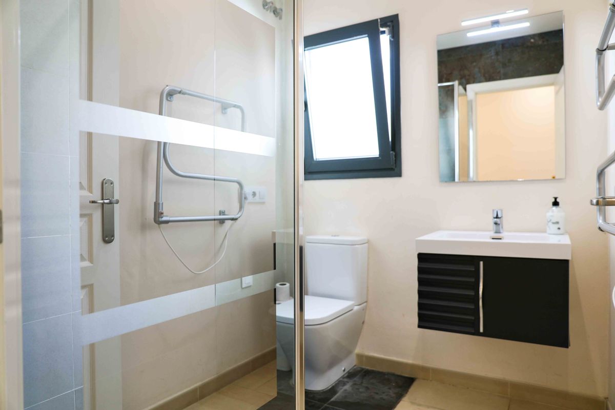 Salle de bain moderne équipée d'une douche avec paroi en verre dépoli, d'un meuble vasque suspendu noir et d'un radiateur sèche-serviettes.